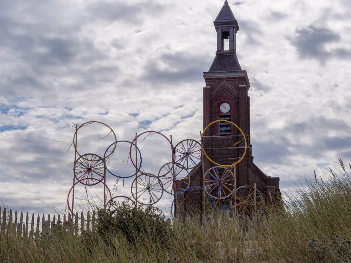 Église en bord de mer entourée d’oyats avec des cerceaux colorés en guise de décoration au premier plan.